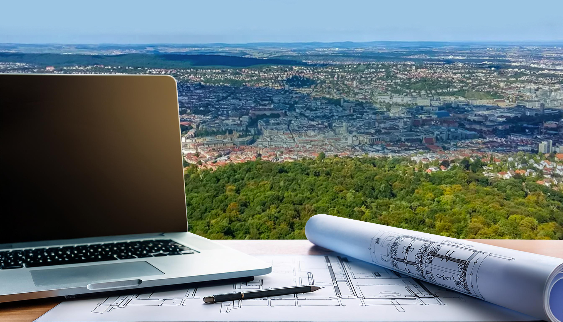 Im Vordergrund ist ein Laptop mit Bauplänen un im Hintergrund ist die Stadt Stuttgart zu sehen.