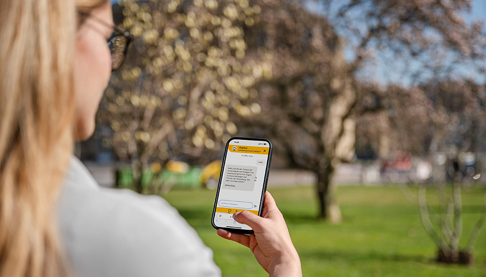 Eine Frau schaut im Schlossgarten in ihr Smartphone, wo der Chatbot der Stadt Stuttgart zu sehen ist.