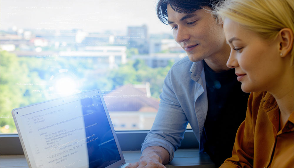 Das Bild zeigt eine Frau und einen Mann, die zusammen an einem Laptop arbeiten. Auf dem Bildschirm sind Codezeilen sichtbar. Um sie herum werden grafische Elemente eingeblendet. Im Hintergrund ist eine Stadtlandschaft zu sehen. Die beiden scheinen konzentriert und interessiert.